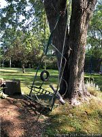 Full view of chair hanging from tree showing seat, frame and support bar