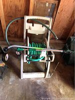 Photo of plastic hose reel with green garden hose and two magic wand sprayers attached, showing front and side views of the reel.