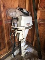 White vintage Viking 55 HP outboard motor with throttle control cables hanging, stored in wooden shed