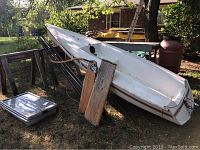 White hull and cockpit on sawhorses with mast sections and boom leaning alongside