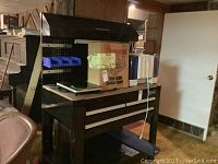 Overall view of the black metal workbench with pegboard, overhead shelf, bench surface and tool chest drawers