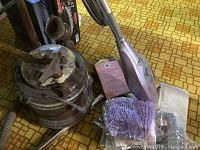 Filter Queen vacuum cleaner canister, hose, and accessories visible with Shark steam mop in front on patterned floor.