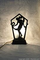 Front view of Art Deco lamp showing silhouette of nude dancing lady with scarf on glass panel behind metal frame.