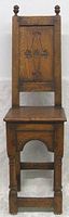 Front view of the antique English oak hall chair showing carved Gothic style panel on the backrest with finial knobs and solid wood seat.