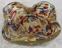 Top-angle view showing the organic freeform shape with clear glass casing and colorful millefiori floral patterns scattered beneath the surface along with gold aventurine flecks.