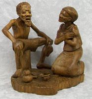 Front angled view of the carved wood sculpture of a seated man and kneeling woman, showing details and base.