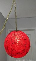 Red spherical hanging lamp with spaghetti-like texture and black loops, shown hanging from gold chain against white background