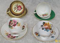 Four antique English porcelain cups arranged upright with matching saucers underneath, showing floral patterns and gold trim.