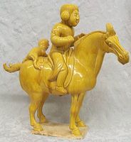 Front-left side view of the yellow glazed pottery statue showing woman on horse with monkey