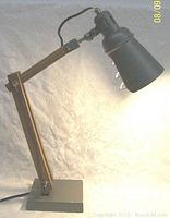 Front angled view of the lamp turned on showing the metal shade and wooden arm articulation.