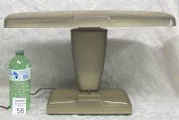 Front view of the lamp alongside a water bottle for scale, showing the full structure including the base, tapering column, and wide fluorescent shade.