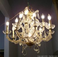 Front view of brass and glass chandelier with eight candle-shaped bulbs and hanging crystal drops, illuminated.