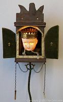 Front view of the antique surreal doll head in the wooden box with green velvet doors open, showing lit glowing eyes and beaded tears.