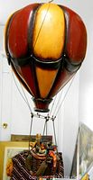 Side view of vintage hot air balloon mobile with yellow and red panels and hanging basket with passengers.