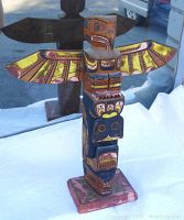 Front and angled views of a carved wooden Haida totem pole showing detailed paintwork on wings and body with visible base wear.