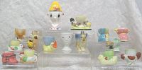 Front view of all 15 vintage figural egg cups arranged on clear risers showing various animal and figure designs.