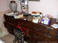 Full view showing wooden dresser with multiple boxes, jewelry organizer, jewelry stand with earrings, and other costume jewelry pieces spread on top of the dresser.