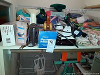 Photo showing an assortment of items on a shelf including iron, iron cord, belt, water filter box, clipper, and cloths.