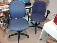 Two blue office chairs with five-star wheeled bases and adjustable armrests placed on carpeted floor, one with patterned fabric and one with solid blue upholstery.