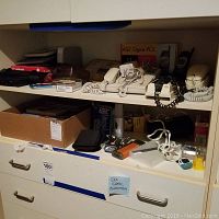 Shelf with vintage phones, flashlights, tools, and boxes containing kits and books