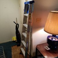 Photo of the 6-foot tall Werner metal ladder leaning against a wall indoors near furniture and a lamp.