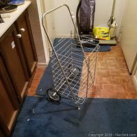 Metal rolling cart with white or silver wire frame basket, two wheels, and handle.