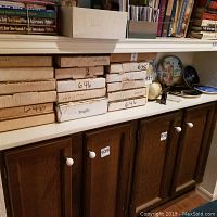 Stack of multiple boxes labeled 646 containing fragile decorative plates stored on countertop beneath bookshelves.