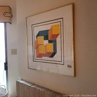 Square framed geometric art piece hanging on wall above brick mantle, gold-tone frame