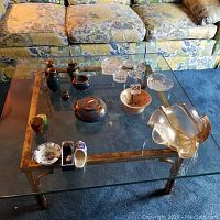 View of the glass coffee table surface holding the assortment of glass and ceramic bowls and decorative items.