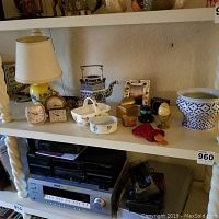 Yellow ceramic lamp, alarm clocks, ceramic teapot, decorative frame, and flower vase arranged on a white shelf