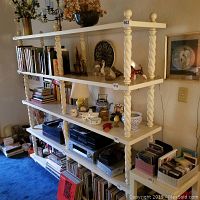 Front view of 4-tier white wooden shelf showing books, decorative items, and spiral carved columns, minor scratches visible