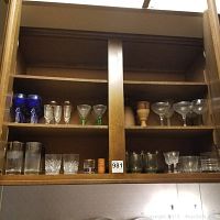 Display of shelves with various glassware and terracotta goblets including blue wine glasses, etched bride and groom glasses, cocktail glasses, and clear tumblers.