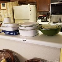 Full lot of white Corningware baking dishes stacked and green Pyrex nested mixing bowls set on kitchen counter.