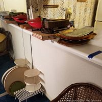 Wide view of lot on white countertop showing red electric wok, wooden, glass warming trays, and some wire racks and trays.