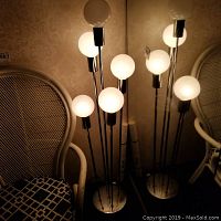 Overall view of two chrome multi-arm floor lamps against wallpapered wall with wicker chair