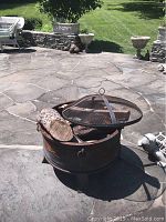 Steel fire pit with mesh cover and fire logs on a stone patio in bright outdoor lighting.