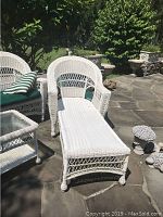 Full angled photo showing a white plastic resin wicker lounge chair outdoors on stone patio, with green and white striped cushions visible on adjacent chair.