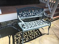 Metal garden bench with ornate floral and leaf cutout design, showing some paint chipping and bent legs.