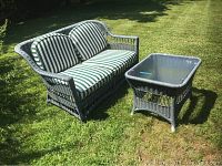 Outdoor view of gray wicker loveseat with green and white striped cushions next to matching glass-top cocktail table on grass.