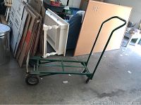 Side view of green metal folding hand truck extended flat on ground