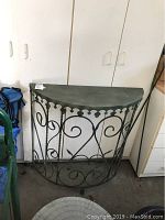Front view of demilune metal table showing the flat half-moon top and ornate scroll metal base