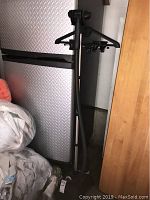 Full view of the black garment steamer standing on floor next to a metal cabinet in a garage.