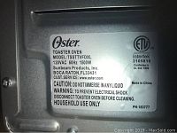 Close-up of Oster toaster oven model label showing model TSSTTVFDXL, 120VAC, 1500W, caution and warning information.