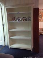 Front view of white bookcase with four shelves partially filled and ruler standing beside it.