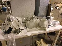 Pair ceiling chandeliers with ribbed clear glass shades, metal polished chrome canopies, hanging chains and power cables with neon ballasts, placed on a table with additional glass components.