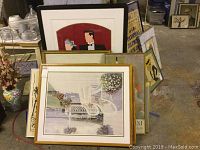View of several framed prints and posters stacked together showing a variety of styles including floral and patio scenes