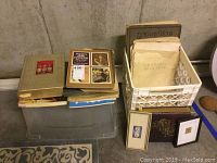 Full view of vintage books, loose antique plates in plastic crate, and small framed art pieces arranged on the floor.
