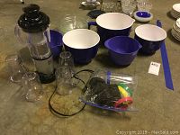 Several clear glass nesting bowls and blue melamine bowls arranged on a surface with Magic Bullet Express blender and accessories nearby.