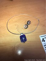 Photo of Italian sterling silver necklace with a blue stained glass pendant and floral patterned earrings on a wooden surface.