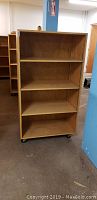 Photo of single wooden bookcase showing three shelves and casters at bottom, medium wood finish.